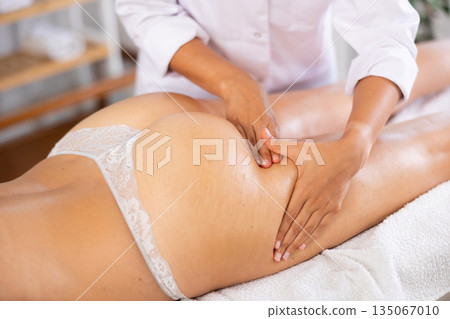 Female masseur performs stroking during spa procedure of thigh area for girl, close up Female masseur performs stroking during spa procedure of thigh area for girl, close up 135067010