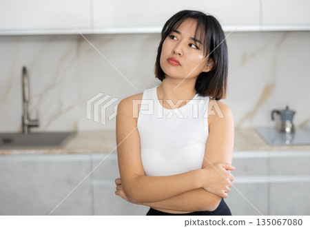 Sad young Asian girl standing at table in the kitchen 135067080