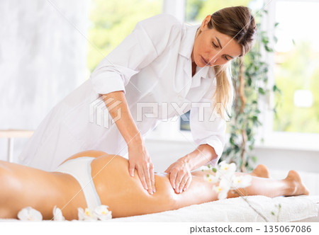 Female masseur performs stroking during spa procedure of thigh buttocks area for girl 135067086