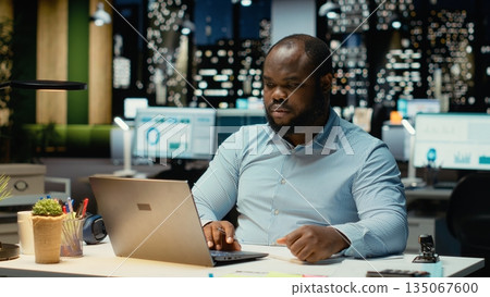 Black office employee ripping a piece of paper after making a mistake, restarting his task in anger and tearing up the page sheet. Discontent guy writes a typo while transcribing. Black office employee ripping a piece of paper after making a mistake, restarting his task in anger and tearing up the page sheet. Discontent guy writes a typo while transcribing. 135067600