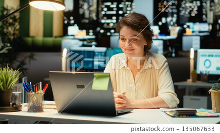 Professional woman sits in front of laptop during a teleconference, engaged in digital discussion. Interacting with participants, demonstrating adaptability in networking session. Camera B. Professional woman sits in front of laptop during a teleconference, engaged in digital discussion. Interacting with participants, demonstrating adaptability in networking session. Camera B. 135067633