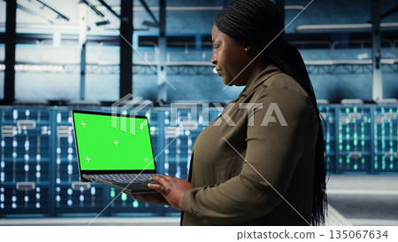 Developer in data center using green screen laptop to upgrade systems for increased stability. IT expert in server farm configuring hardware with mockup notebook for optimum performance, camera A 135067634