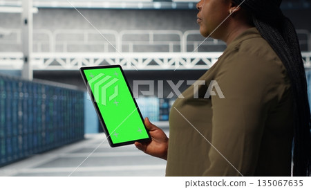 Developer in data center using isolated screen tablet to upgrade systems for increased stability. IT expert in server farm configuring hardware with chroma key device for optimum performance, camera B 135067635