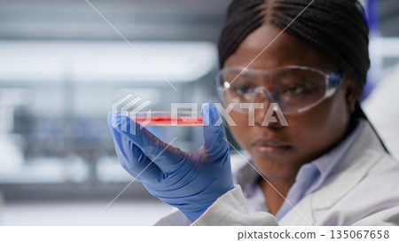Researcher inspects Petri dish with magnifying glass during lab experiment. Cellular investigation and molecular biology analysis support genetics research and advanced medical science. 135067658
