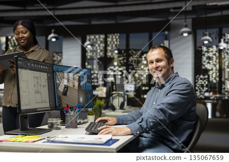 Portrait of engineer working on floor plan interior design at computer, using architectural software and blueprints for 3D render of a home interior. Configure furniture and other elements. Portrait of engineer working on floor plan interior design at computer, using architectural software and blueprints for 3D render of a home interior. Configure furniture and other elements. 135067659