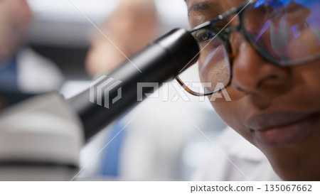 Close up of researcher focusing on a microscope with samples in chemistry lab. Using observation tool with tray for diagnostics, molecular analysis and discovery. Optics in bioscience. Close up of researcher focusing on a microscope with samples in chemistry lab. Using observation tool with tray for diagnostics, molecular analysis and discovery. Optics in bioscience. 135067662