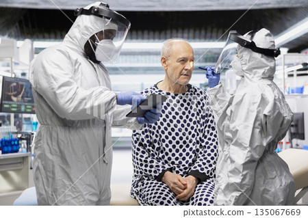 Healthcare professionals in hazmat suits perform diagnostics on patient infected with dangerous virus, studying immunity and vaccination response in a secure biocontainment environment. 135067669