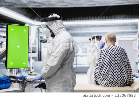 Green screen in vertical position next to doctor in hazmat suit conducting pharmacology experiments and developing vaccines for infection control and biotechnological advancement. 135067688