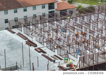 Construction works on metal walls of commercial building. Blue collar workers at large site with scattered equipment. Development of residential housing in America. Real estate market in USA 135068308