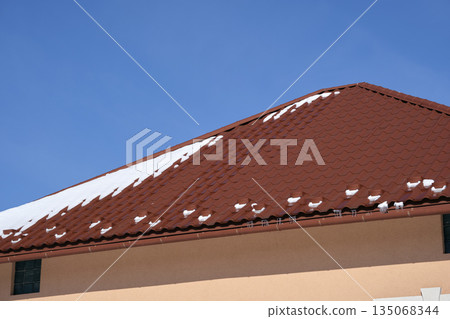 Closeup of house roof top covered with snow in cold winter. Tiled covering of building in wintertime weather Closeup of house roof top covered with snow in cold winter. Tiled covering of building in wintertime weather 135068344