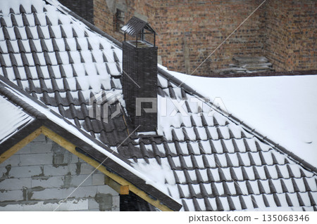 Closeup of house roof top covered with snow in cold winter. Tiled covering of building in wintertime weather Closeup of house roof top covered with snow in cold winter. Tiled covering of building in wintertime weather 135068346