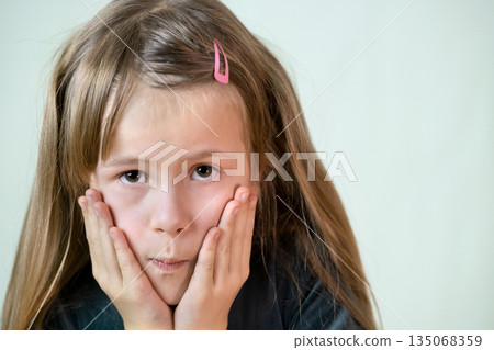 Close-up portrait of little child girl with long hair covering her mouth with hands. Close-up portrait of little child girl with long hair covering her mouth with hands. 135068359
