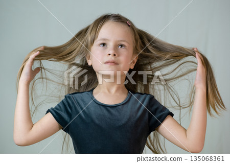 Close-up portrait of happy smiling little girl holding in hands her long hair. 135068361