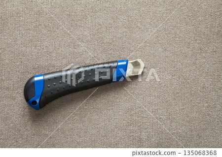 Close-up of isolated stationery retractable metallic knife with sharp blade on light cloth copy space background. 135068368
