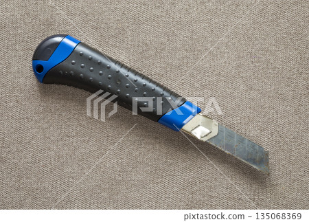 Close-up of isolated stationery retractable metallic knife with sharp blade on light cloth copy space background. Close-up of isolated stationery retractable metallic knife with sharp blade on light cloth copy space background. 135068369