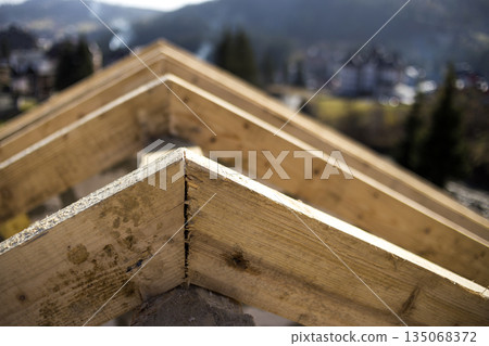 Close-up detail of roof frame of rough wooden lumber beams on background of misty mountain landscape in ecological area. Building, roofing, construction and renovation concept. 135068372