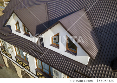 Close-up aerial view of building attic rooms exterior on metal shingle roof, stucco walls and plastic windows. 135068380