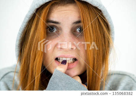 Close up portrait of scared young redhead woman wearing warm hoodie pullover. 135068382