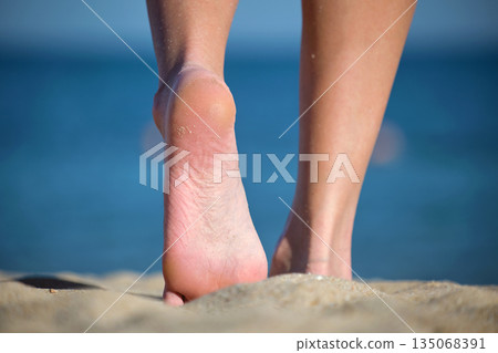 Close up of female feet walking barefoot on white grainy sand of golden beach on blue ocean water background 135068391