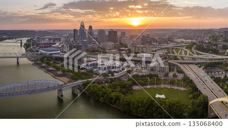 Cincinnati city in state of Ohio with brightly illuminated high skyscraper buildings in downtown district. American megapolis with business financial district at sunset Cincinnati city in state of Ohio with brightly illuminated high skyscraper buildings in downtown district. American megapolis with business financial district at sunset 135068400
