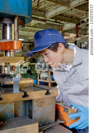 Male worker operating a press machine in a factory Male worker operating a press machine in a factory 135070537
