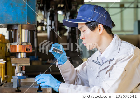 工廠裡,一名男工人正在操作沖壓機。 工廠裡,一名男工人正在操作沖壓機。 135070541