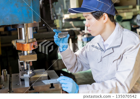 工廠裡，一名男工人正在操作沖壓機。 135070542