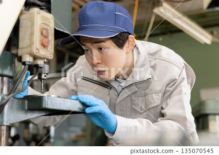 Young man working on a drill press in a factory Young man working on a drill press in a factory 135070545
