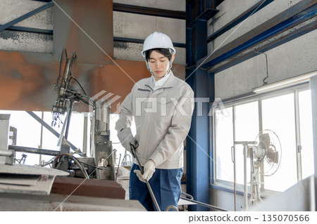 Male worker working in an aluminum melting furnace at a factory Male worker working in an aluminum melting furnace at a factory 135070566