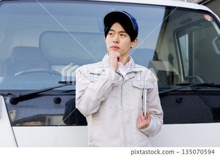 一名送貨員憂心忡忡地站在一輛卡車前 一名送貨員憂心忡忡地站在一輛卡車前 135070594