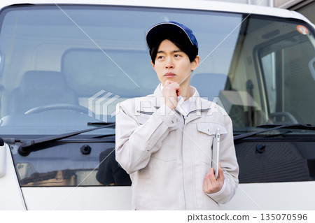 一名送貨員憂心忡忡地站在一輛卡車前 一名送貨員憂心忡忡地站在一輛卡車前 135070596