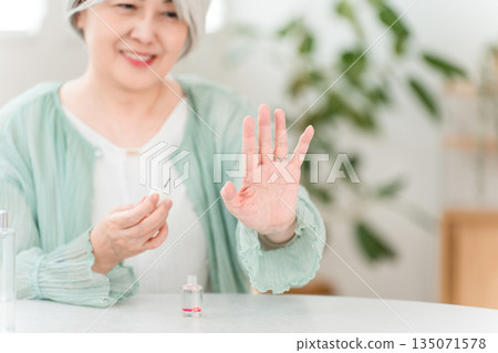 A gray-haired senior woman moisturizing her nails with nail polish and nail oil A gray-haired senior woman moisturizing her nails with nail polish and nail oil 135071578