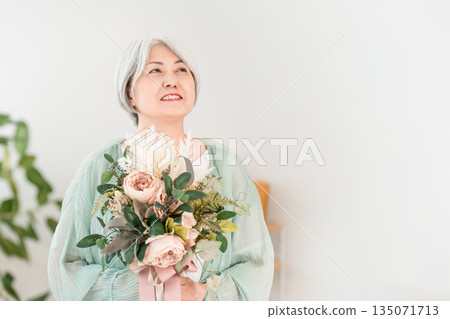 一位頭髮花白的老婦人在家裡的客廳裡手捧一束鮮花。 135071713