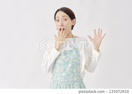 一位穿著圍裙、站在白色背景前的女士，顯得驚訝。 135072658