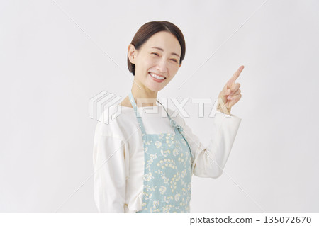 一位身穿圍裙的女子指向右側，白色背景 135072670
