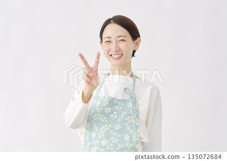 一位身穿圍裙的女子在白色背景上比劃和平手勢 135072684