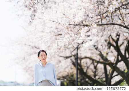 A young woman posing under a row of cherry blossom trees. Lifestyle image A young woman posing under a row of cherry blossom trees. Lifestyle image 135072772