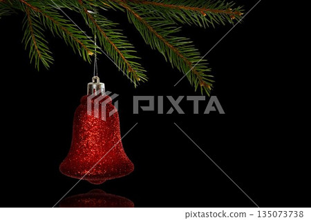 Red glitter bell ornament is hanging from pine branch in 3D with silver cap, black backdrop 135073738