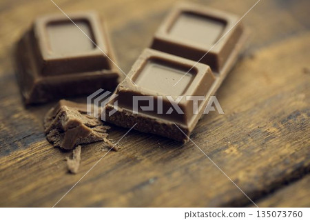 Flat design milk chocolate squares are resting on wooden surface with scattered shavings and crumbs 135073760