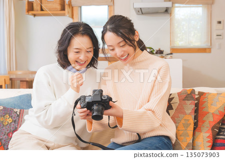 A mother and daughter happily talk about their travel memories while looking at photos in the living room A mother and daughter happily talk about their travel memories while looking at photos in the living room 135073903