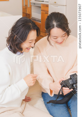 一對母女在客廳裡一邊看著照片，一邊愉快地談論著她們的旅行回憶。 135073907