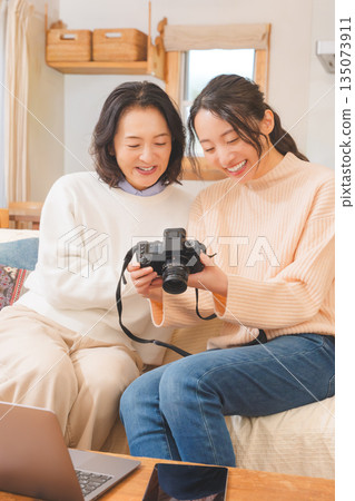 一對母女在客廳裡一邊看著照片，一邊愉快地談論著她們的旅行回憶。 135073911