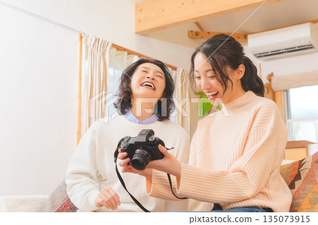 A mother and daughter happily talk about their travel memories while looking at photos in the living room A mother and daughter happily talk about their travel memories while looking at photos in the living room 135073915