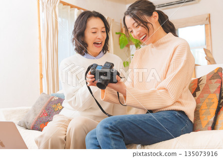 A mother and daughter happily talk about their travel memories while looking at photos in the living room A mother and daughter happily talk about their travel memories while looking at photos in the living room 135073916