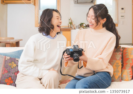 A mother and daughter happily talk about their travel memories while looking at photos in the living room A mother and daughter happily talk about their travel memories while looking at photos in the living room 135073917