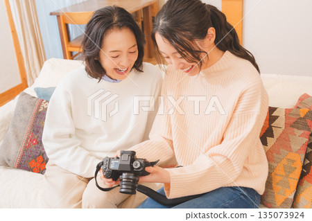 A mother and daughter happily talk about their travel memories while looking at photos in the living room 135073924