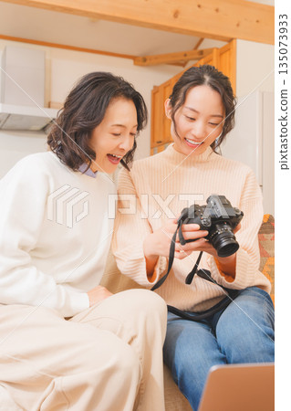 A mother and daughter happily talk about their travel memories while looking at photos in the living room 135073933