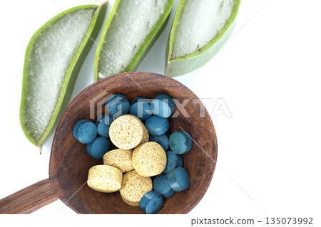 Natural aloe vera slices and colorful pills in a wooden spoon on white background 135073992