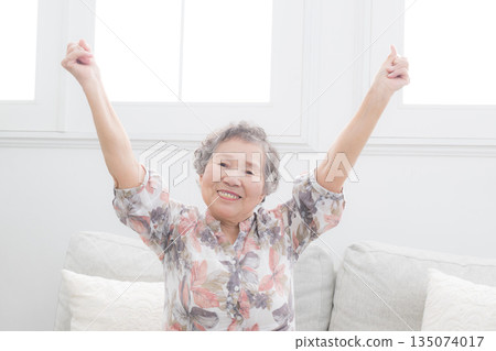 An elderly woman raising both hands in a cheery pose. An image of health and stretching to feel refreshed. An elderly woman raising both hands in a cheery pose. An image of health and stretching to feel refreshed. 135074017