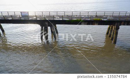 Close Up of Old Bridge Pillars in Muddy River Water with Sunlight Reflection 135074784